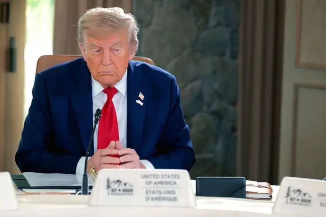 The president of the United States, Donald Trump, attends a meeting with the G7 leaders at the G7 leaders summit, on June 16, 2025, in Kananaskis, Alberta. Dressed in a navy blue suit, red tie and a US pin, sits at the table with crossed hands